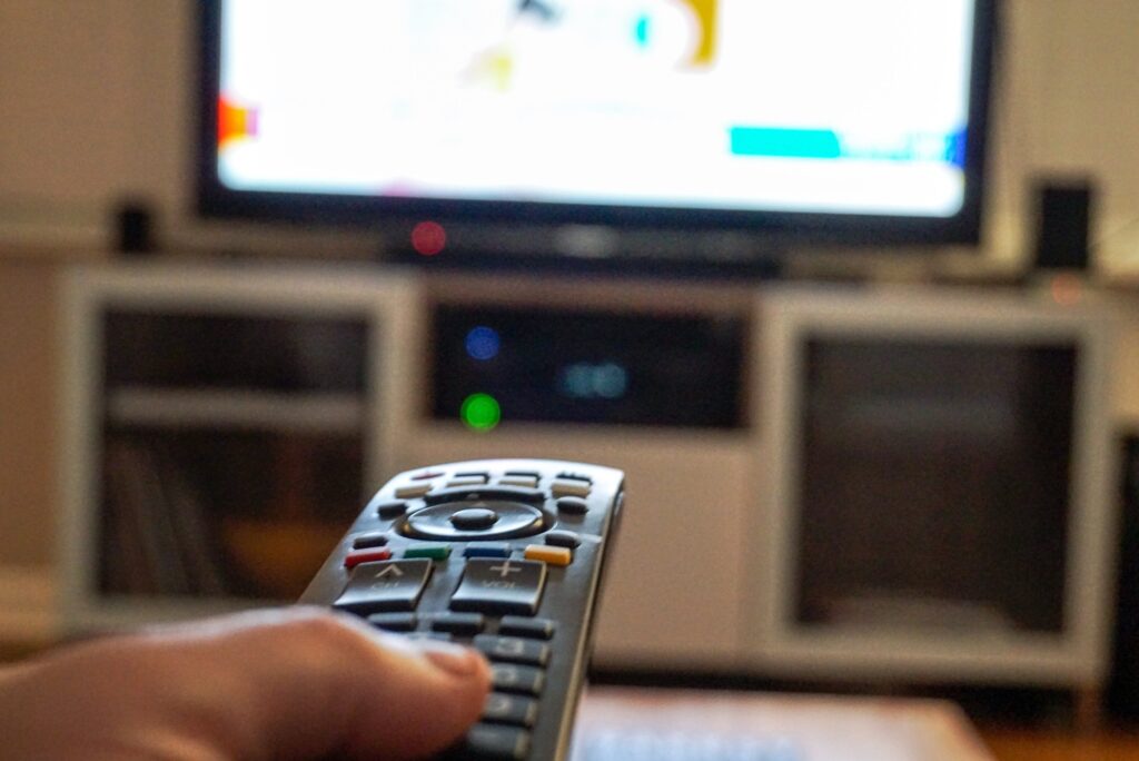 A hand holding a remote control aiming it at a television trying to change channels